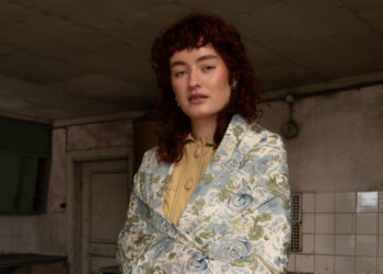 Woman with curly hair in vintage setting, wearing floral blazer and yellow blouse.